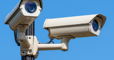 Dos cámaras de vigilancia o control de velocidad montadas en un poste metálico, con lentes orientadas en distintas direcciones, contra un cielo azul despejado.