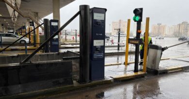 Terminal de cobro automático de peaje Cooresur con barrera levantada y semáforo en verde, operada por un empleado con chaleco reflectivo. Estación bajo techo en día lluvioso con edificios al fondo. AUTOPISTA RICCHERI
