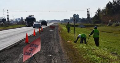 Trabajadores viales en banquina de ruta bonaerense señalizada con cartel "Zona de Obra" y conos naranjas.