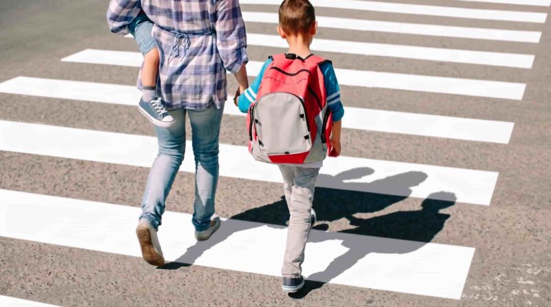 Adulto y niños cruzando por senda peatonal tomados de la mano en día soleado.