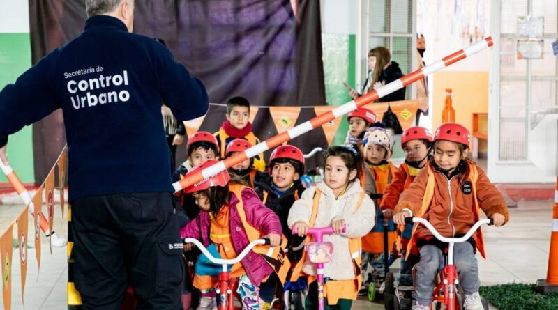 Niños con cascos y chalecos de seguridad en fila sobre triciclos, durante un taller de educación vial escolar.