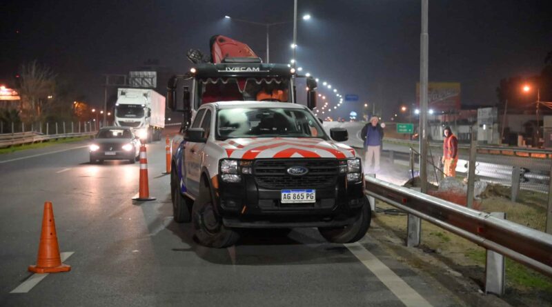Operativo nocturno de obras viales en la Autopista Panamericana: una camioneta Ford con señalización vial naranja y blanca corta un carril, flanqueada por conos, mientras una grúa trabaja al fondo y operarios realizan tareas sobre la banquina.