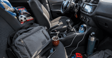 Interior de un automóvil desordenado con un mate, un termo, una mochila, juguetes y una pelota de fútbol sobre los asientos y la consola central.