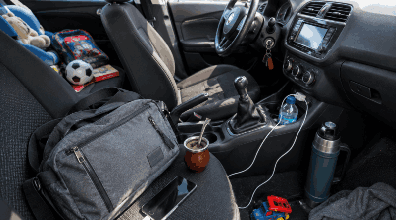 Interior de un automóvil desordenado con un mate, un termo, una mochila, juguetes y una pelota de fútbol sobre los asientos y la consola central.