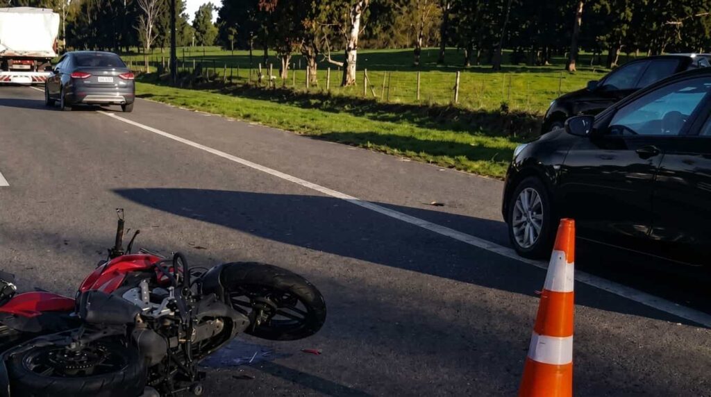 Motocicleta siniestrada sobre la calzada de la Ruta 2, con cono de señalización y vehículos detenidos tras un choque.