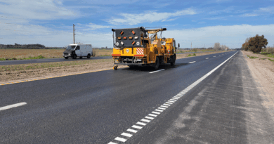 Máquina demarcadora de pavimento trazando líneas blancas sobre asfalto nuevo en una ruta de la provincia de Buenos Aires, con campos y cielo despejado al fondo.